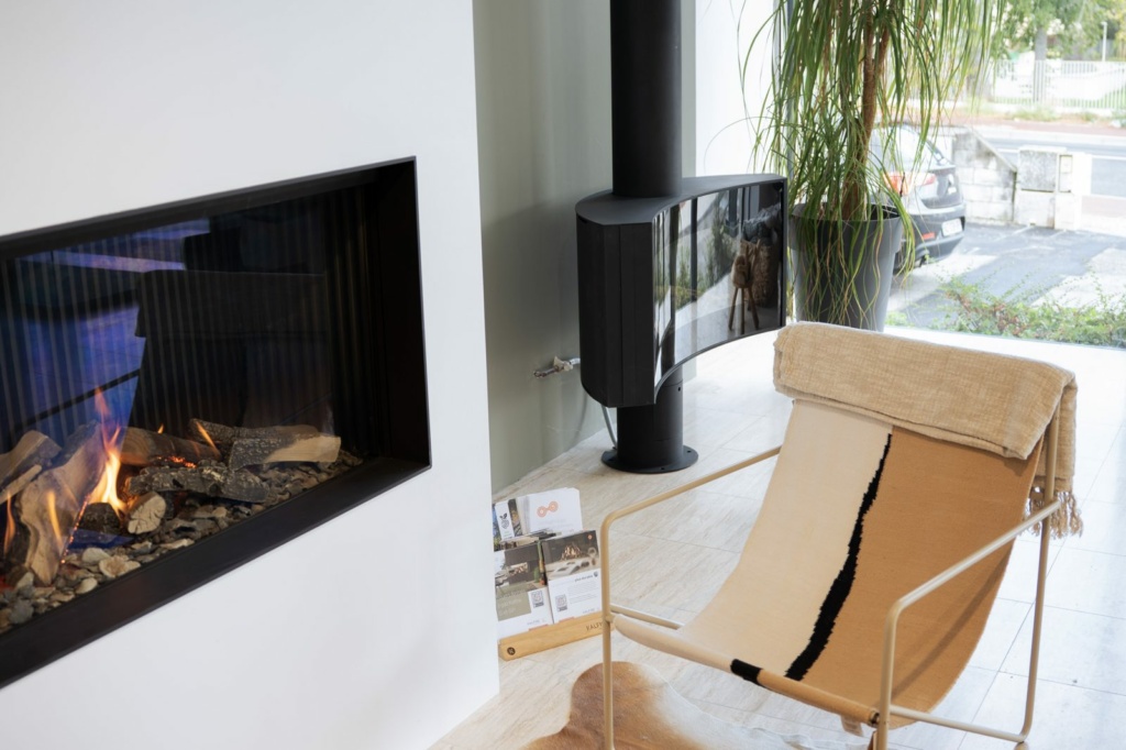 Foyer gaz linéaire et poêle suspendu devant la baie du showroom Sparte à Toulouse